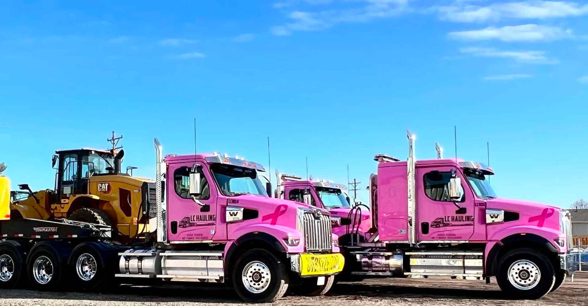 LC hauling pink trucks with CAT machines in tow
